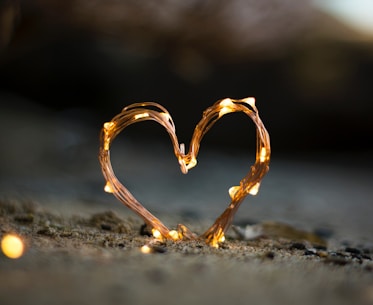 close-up photography of heart shaped fairy lite on brown sand