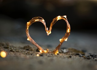 close-up photography of heart shaped fairy lite on brown sand