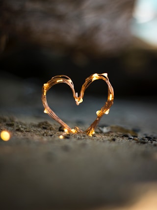 close-up photography of heart shaped fairy lite on brown sand