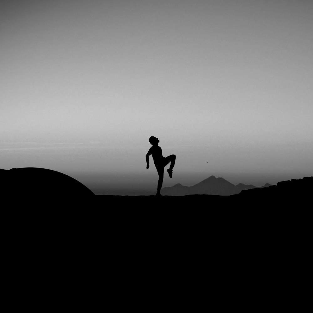silhouette photography of man standing with one leg on ground
