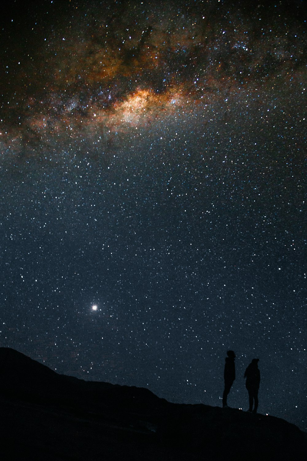 silhouette di due persone in piedi sotto il cielo della Via Lattea durante la notte