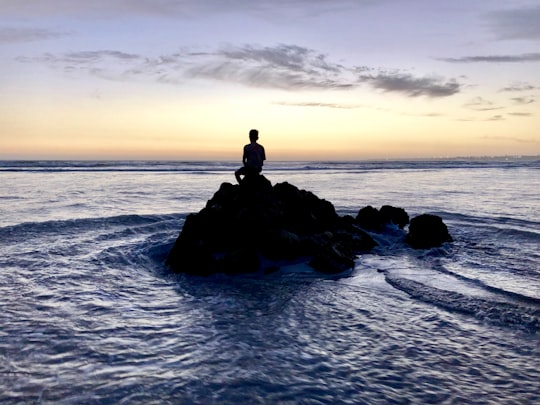 silhouette photo of person sitting on rock formation in between body of water in Hermanus South Africa