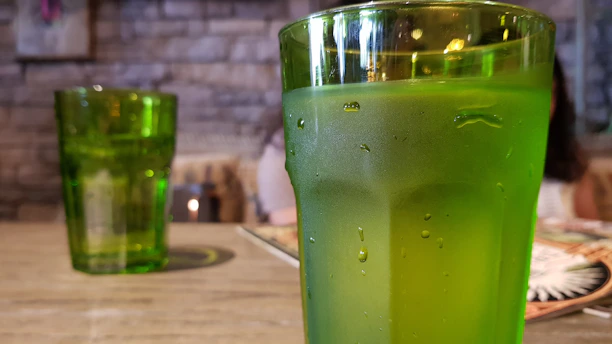Close-up of a chilled glass of gosattuu with condensation, surrounded by fresh roasted chana and green leaves on a rustic wooden table.