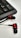 A set of black and red in-ear headphones positioned on a white surface next to a black computer keyboard. The headphones have a distinctive red ring design around the earbuds and a flat cable extending from them.