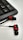 A set of black and red in-ear headphones positioned on a white surface next to a black computer keyboard. The headphones have a distinctive red ring design around the earbuds and a flat cable extending from them.