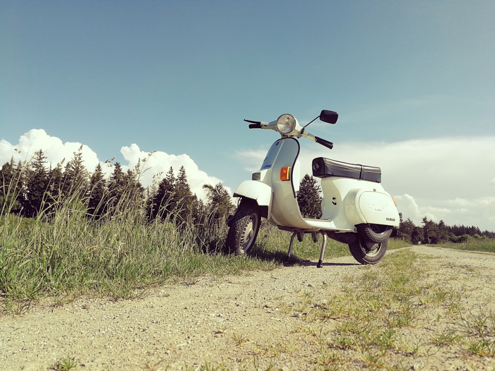 white motor scooter parked beside grass field on outdoors
