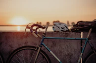 Bicycle leaning against a rustic wall with a helmet and a reusable water bottle hanging from the handlebars.