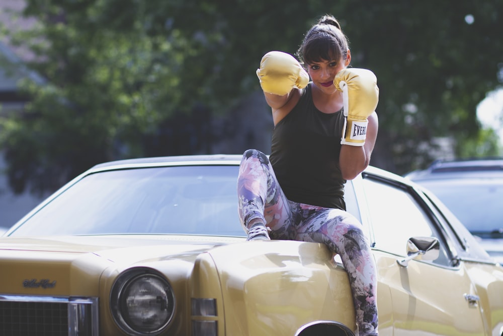 woman sitting on yellow car while punching air