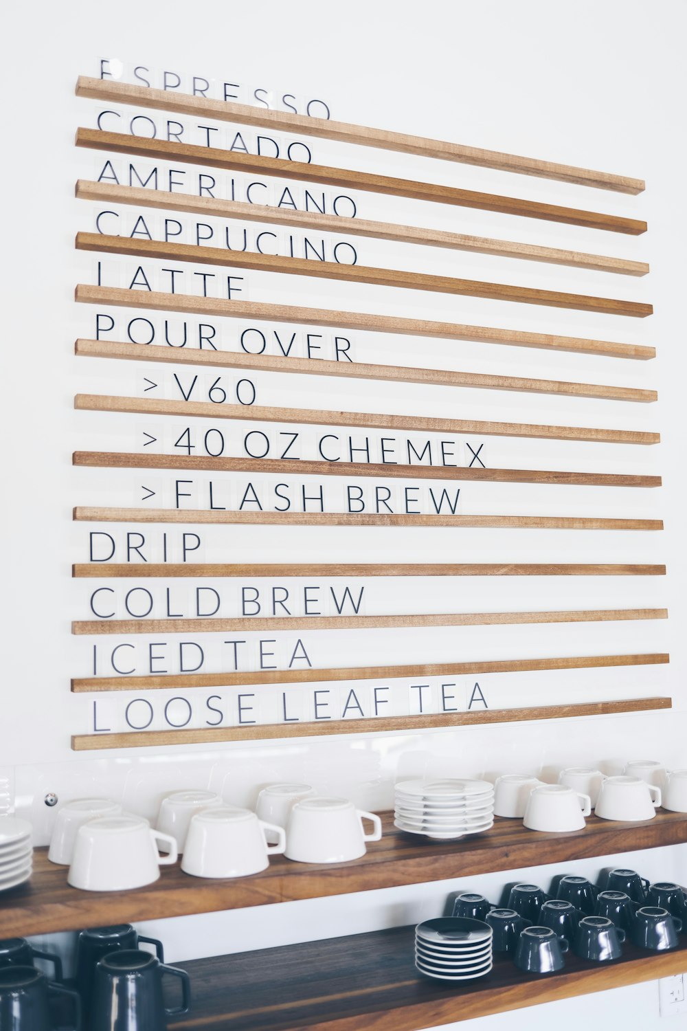 white-and-black ceramic dinnerware sets piled on brown shelf beside wall