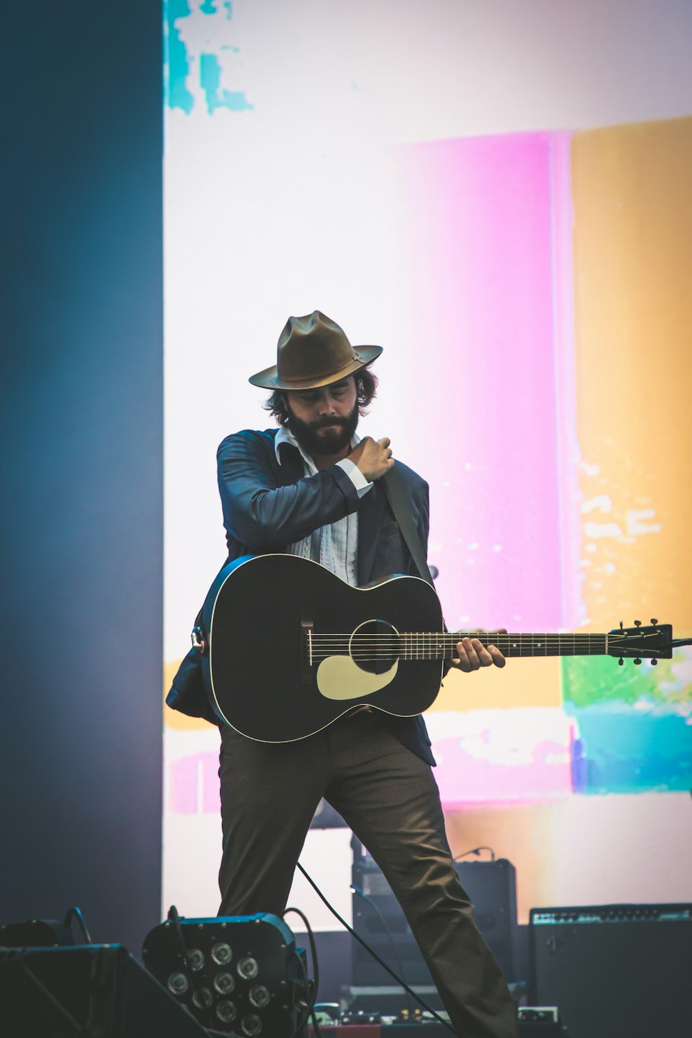 man in black long sleeve shirt and black pants wearing black hat holding brown acoustic guitar