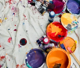 assorted-color paints and paintbrushes on white tarp