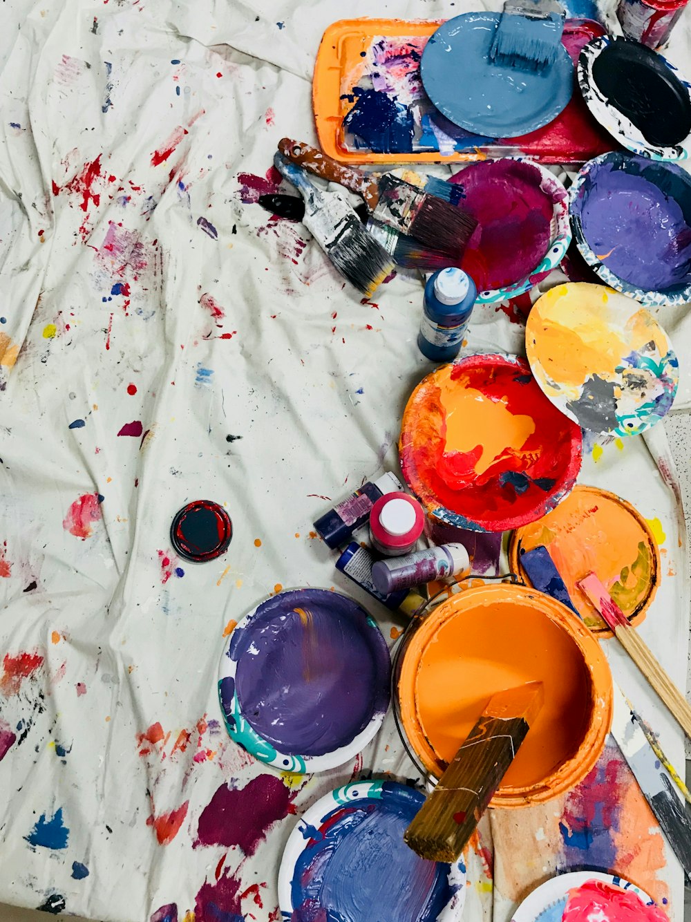 assorted-color paints and paintbrushes on white tarp