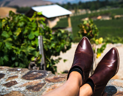 Handmade leather boots resting beside a saddle in a sunlit barn.