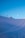 A serene alpine landscape with a snow-covered slope under a clear blue sky. Ski lift chairs are visible on the left near a small wooden cabin, and ski tracks create gentle curves in the snow. The moon is seen in the sky above the scene.