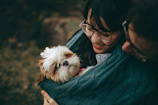 A happy pet parent holding their dog dressed in a cute, colorful dress outdoors