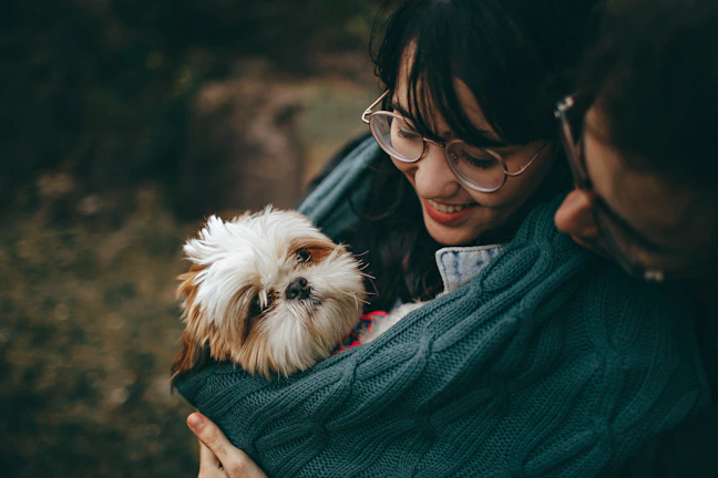 A happy pet parent gently holding their fashionably dressed dog outdoors.