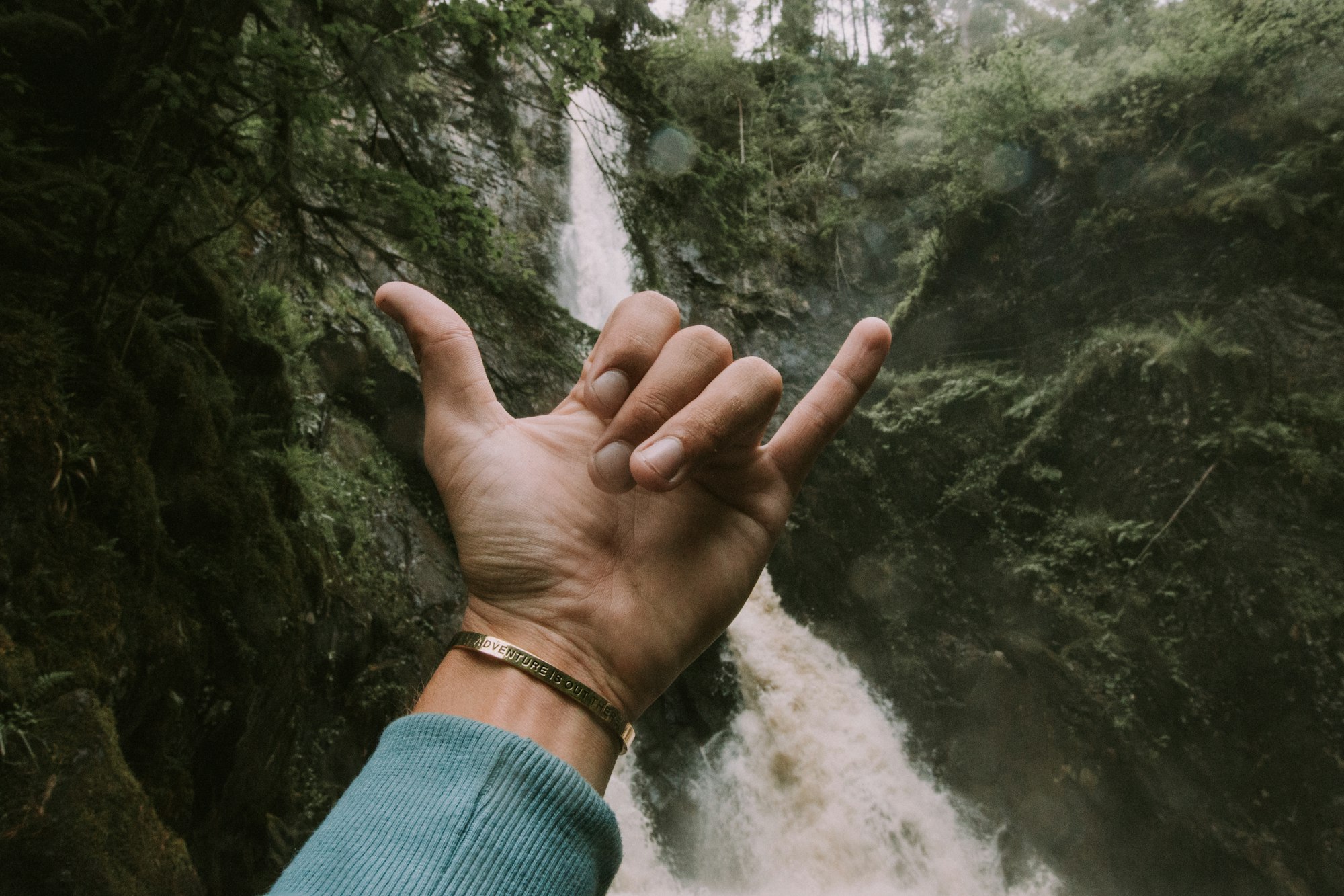 Guy at a waterfall holding up a gesture