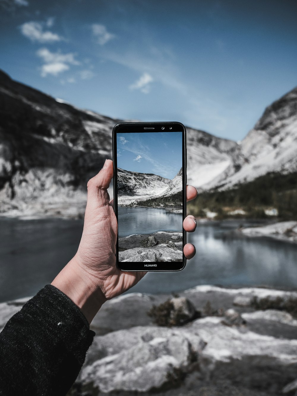Persona sosteniendo un teléfono inteligente negro tomando una foto del lago durante el día