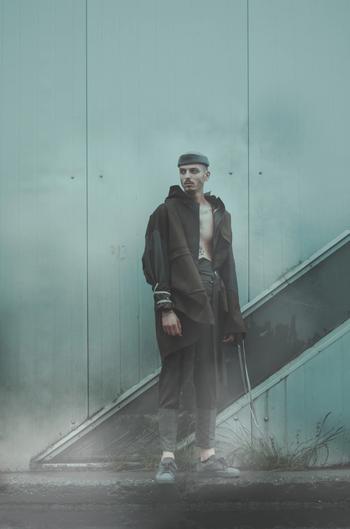 Model in a hooded black overcoat standing by an escalator