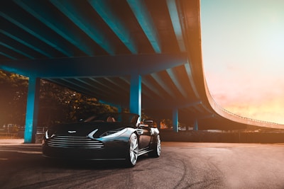 black Aston Martin convertible coupe parked beside blue concrete bridge