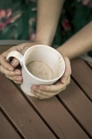 A close-up shot of hands holding a cup of tea, resting gently on a worn wooden table.