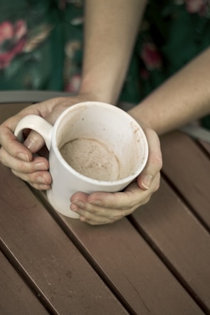 A close-up shot of hands holding a cup of tea, resting gently on a worn wooden table.