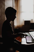 A smiling child playing piano in a cozy, sunlit lesson room decorated with gold and emerald accents.