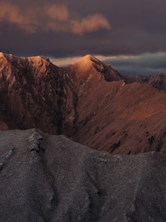 A dramatic mountain landscape with clouds rolling over the peaks at sunrise.
