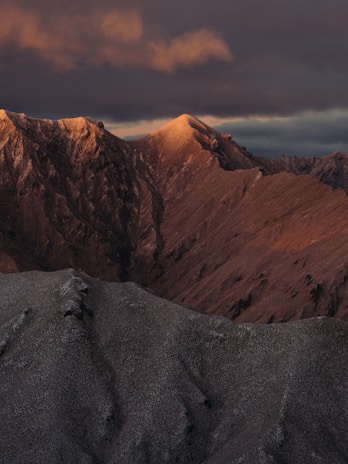 A dramatic mountain landscape with clouds rolling over the peaks at sunrise.