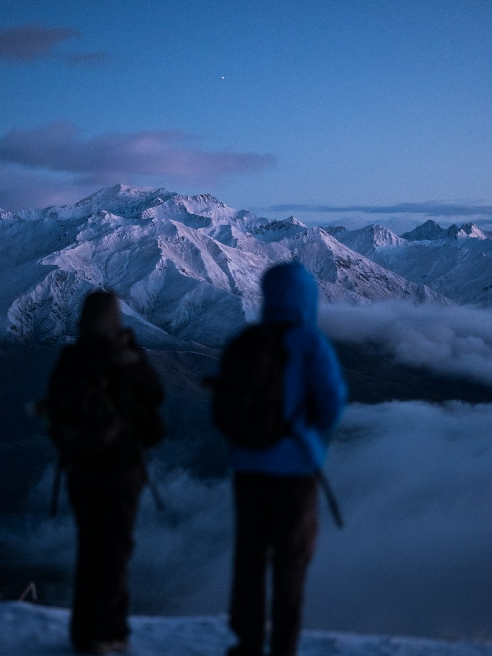 Dos personas de pie en el borde de la montaña con nieblas bajo el cielo azul