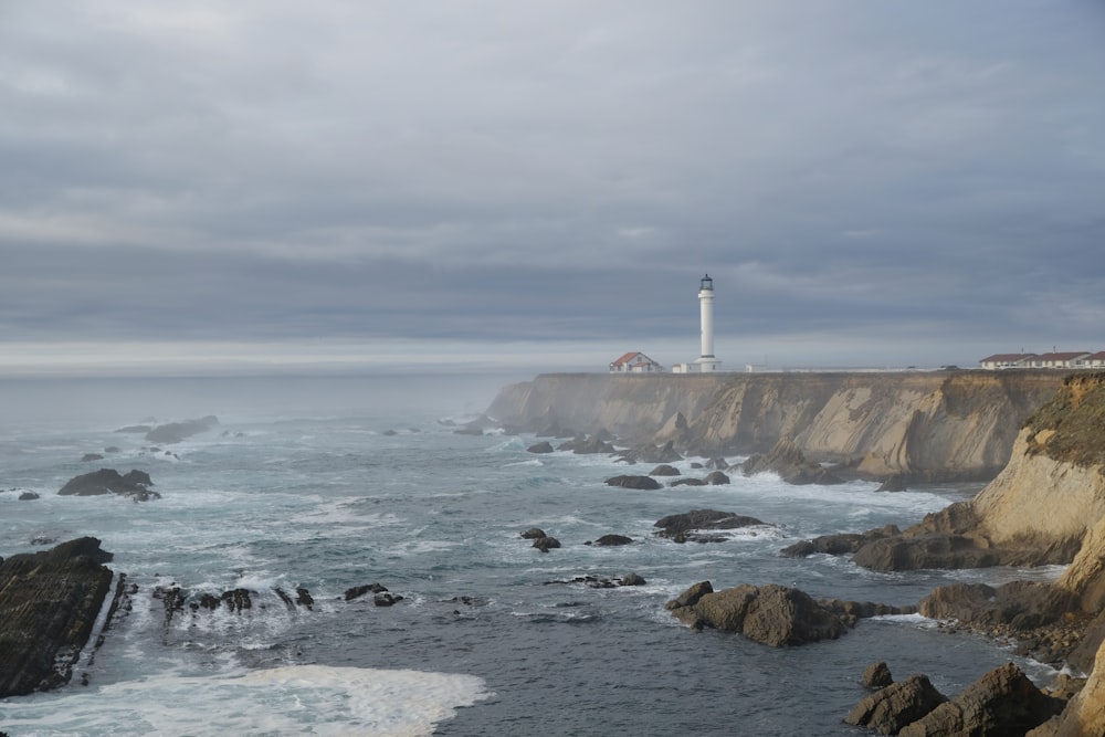 white lighthouse on shore under gray clouds at daytime