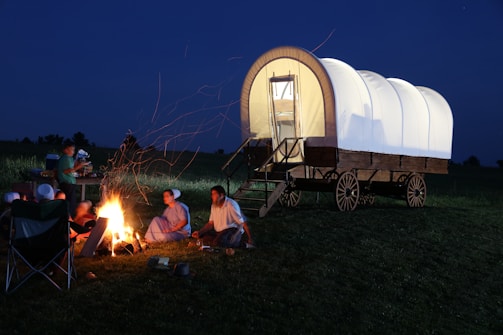 A group of cowboys gathered around a campfire at dusk, sharing stories and laughter under a wide open sky.
