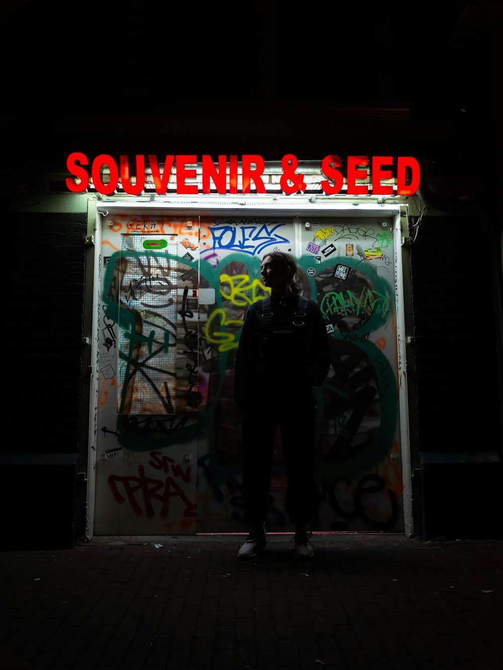 woman standing behind graffiti tagged wall with Souvenir & Seed text overlay