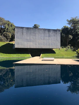Wide shot of a minimalist concrete pavilion surrounded by landscaped greenery.