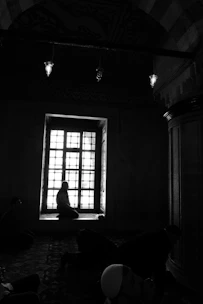 A serene setting with a person sitting quietly in prayer, sunlight streaming through a window.