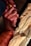 A pair of hands skillfully carves detailed patterns into a block of wood using a carving tool. The wood displays a series of intricate cuts and angled shapes, suggesting an ongoing artistic process. The focus on the hands and tool emphasizes craftsmanship and precision.