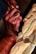 A pair of hands skillfully carves detailed patterns into a block of wood using a carving tool. The wood displays a series of intricate cuts and angled shapes, suggesting an ongoing artistic process. The focus on the hands and tool emphasizes craftsmanship and precision.