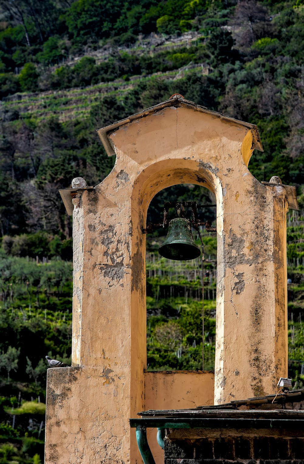 green bell hanging from yellow concrete arch