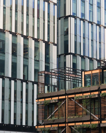 Modern architectural facade blending dark green panels with natural wood textures, surrounded by lush landscaping.