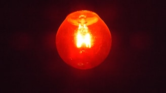 A glowing red light bulb shines brightly against a dark background, illuminating with an intense and warm hue.