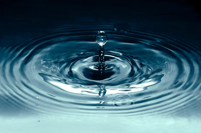 A delicate drop of body oil falling into a clear pool, creating ripples
