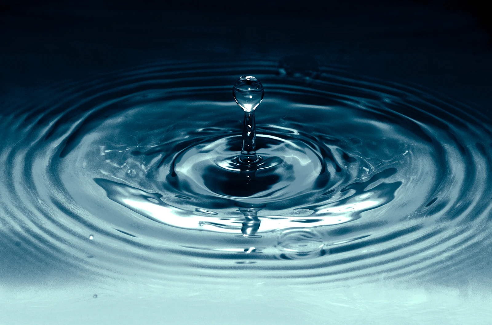 Concentric ripples spreading outward across a dark water surface, evoking compression waves radiating from a source.
