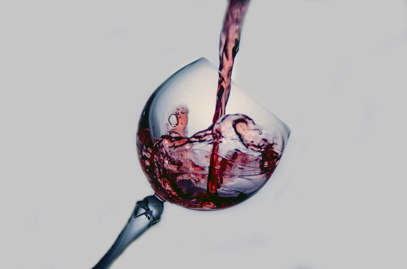 Close-up of a hand pouring deep red wine into a crystal glass, highlighting the rich color and texture.