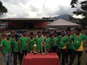 Un grupo de jóvenes con uniformes deportivos verdes y amarillos posan con medallas y trofeos.