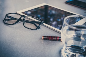 A sleek, portable Rememo device resting on a wooden table beside a pair of reading glasses.