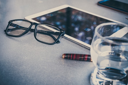 A sleek, portable Rememo device resting on a wooden table beside a pair of reading glasses.