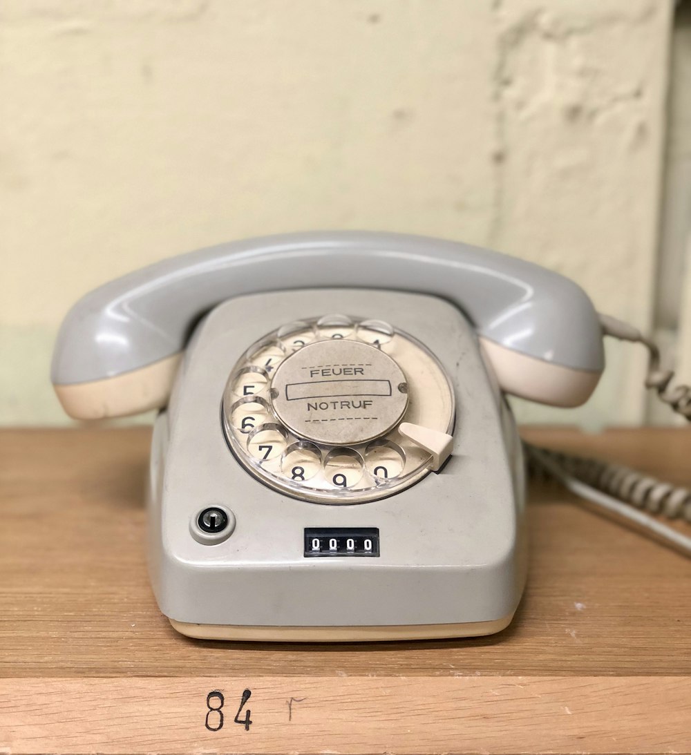 Teléfono de disco gris sobre mesa marrón