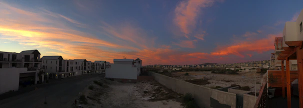 A panoramic view of a newly developed residential area blending green spaces with sleek modern homes under a golden sunset.