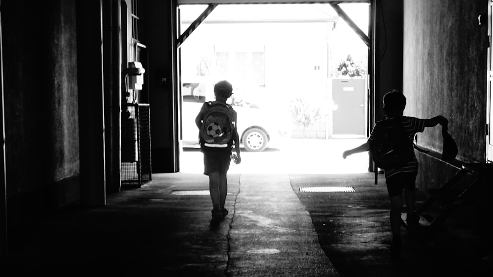 two boys walking in corridor of a building grayscale photo