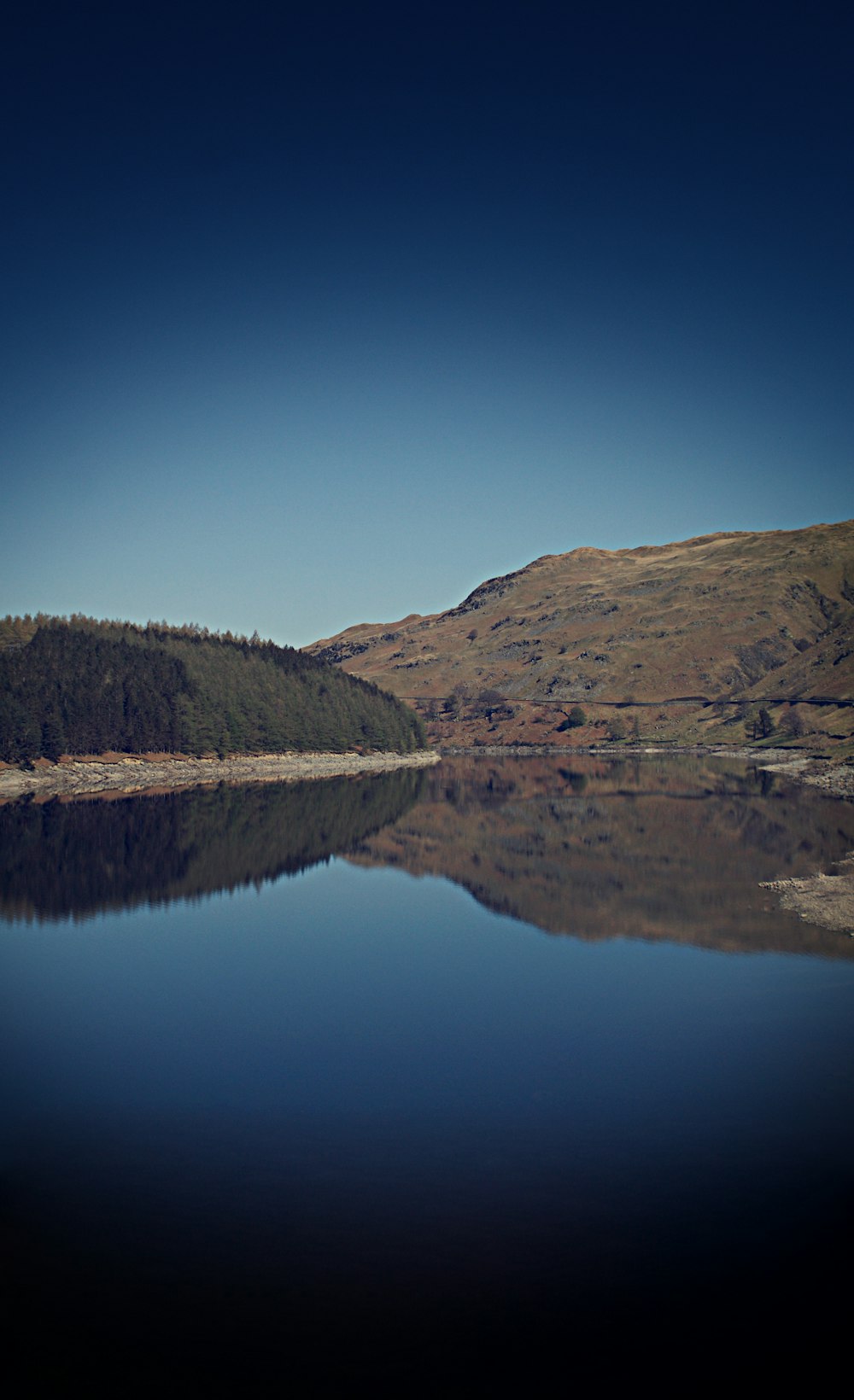 green and brown mountain beside lake under blue sky during daytime